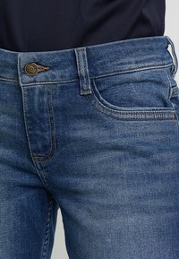 Mörkblå denimjeans med kontrasterande sömmar, klassisk femficksdesign och metalldknapp i midjan. Mjuk textur.