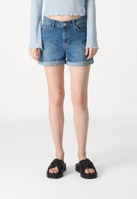 Shorts in denim blu chiaro con vestibilità regolare, orlo arrotolato, cinque tasche e chiusura a zip; indossati con sandali con zeppa neri.