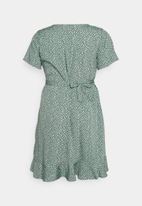 Krátké šaty s krátkými rukávy v světle zelené barvě s černým puntíkovým vzorem, širokým lemem a stahováním v pase. Zobrazený pohled zezadu.