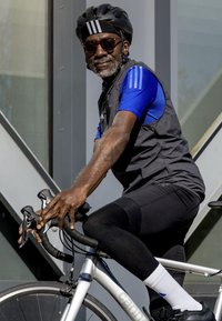 Bicicletta argento con manubri neri; ciclista in pantaloni corti neri e maglietta blu, con occhiali da sole e casco nero, contro uno sfondo moderno.