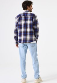 Geruite shirt in wit, marineblauw en lichtblauw, met lange mouwen en een comfortabele pasvorm. Draag het over een lichtblauwe spijkerbroek en beige sneakers.