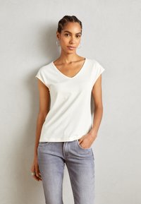 Witte kortemouwen V-hals t-shirt van zachte stof, met een losse pasvorm en subtiele stikdetails, gecombineerd met lichtgrijze jeans.