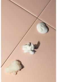 Drei Klöße aus Sahne in unterschiedlichen Texturen und Formen, weiß und cremefarben, auf einer glatten, matten hellrosa Oberfläche platziert.