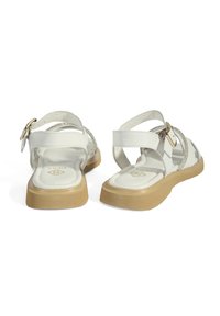 White strappy sandals with a textured upper, clear accents, and a tan rubber sole. Features a small buckle for adjustable fit.