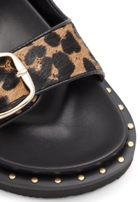 Black sandal featuring a leopard-print strap with a gold buckle, textured upper, and studded black sole.