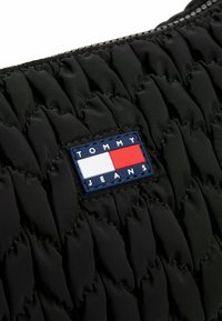Borsa nera in nylon con texture trapuntata, dotata di una toppa con il marchio blu, bianco e rosso riportante la scritta "TOMMY JEANS" sul frontale.