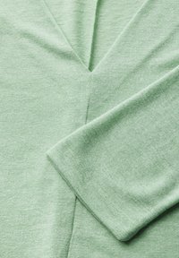 Top de punto suave en verde claro, con escote en V y mangas cortas, que presenta una textura sutil y costuras limpias en los bordes.