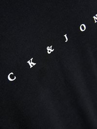 Schwarzes T-Shirt-Gewebe mit weißem Text, der "CK & JON" liest. Nahaufnahme betont die glatte Textur und die kräftige Schrift.