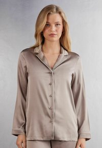 Satinbeige pyjamasammare med långa ärmar, notchade kragar, framknappar och vit passpoal längs kragen och ärmsluten.