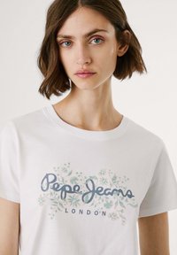 Vit bomull t-shirt med en blommig design i blått och grönt samt texten "Pepe Jeans London". Klassisk rund halsringning och korta ärmar.