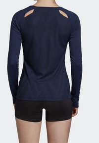 Marinblå långärmad träningströja med nätutskärningar, strukturerad yta och diamantmönster. Kombinerad med svarta shorts.