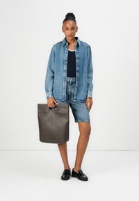 Denim shirt layered over a navy tank, paired with denim shorts. Black loafers and a dark brown leather tote bag with a handle.