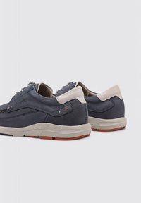 Zapatillas oscuras de cuero liso con detalles en gris claro. Cuentan con puntera redonda, cordones planos y una suela de goma con detalles en naranja.