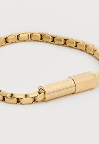 Βραχιόλι με συνδεδεμένους κρίκους σε χρυσό τόνο, με ομαλούς, ορθογώνιους κρίκους αλυσίδας και διακοσμητικό κυλινδρικό κούμπωμα χαραγμένο με το λογότυπο Calvin Klein.