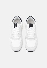 Biało-szary sneaker z materiałami siateczkowymi i zamszowymi, płaskie sznurowadła, czarny akcent na pięcie oraz logo na języku. Zaokrąglony nosek i amortyzowana podeszwa.