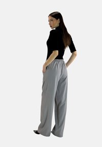 Top corto nero a maniche corte abbinato a pantaloni grigi larghi con vita elastica, tasche laterali e una texture liscia.