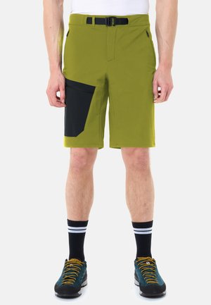 Uomo che indossa pantaloncini verde oliva con una grande tasca laterale nera, calzini neri con strisce bianche e scarpe da trekking turchesi con lacci gialli.