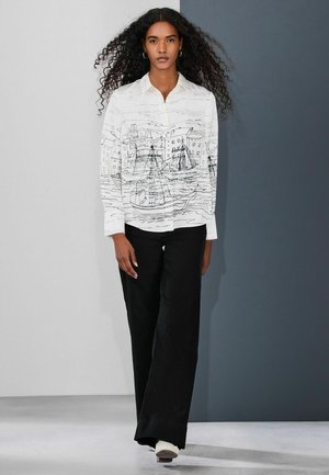 Valkea pitkähihainen napillinen paita, jossa musta rannikkokuvio. Yhdistetty mustiin leveälahkeisiin housuihin ja valkoisiin tennareihin.