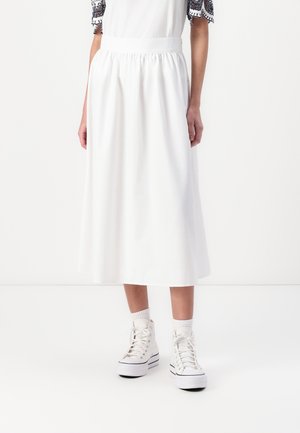 Jupe blanche mi-longue avec taille élastique, présentant une texture lisse. Associée à des baskets montantes blanches et des chaussettes montantes.