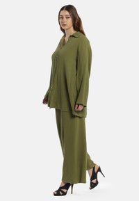 Olivgrön tvådelad outfit gjord av texturerat tyg. Skjortan har en krage och en lös passform; matchad med vida byxor och svarta klackar.