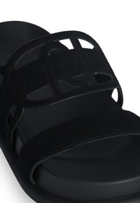 Sandali in suede neri con un design a fascia larga e un accento testurizzato sulla parte superiore, dotati di una suola liscia nera.