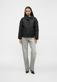 Čierna prešívaná bunda so zipsom vpredu, golierom a dvoma prednými vreckami. Skombinovaná so svetlo šedými nohavicami so rovnými nohavicami a čiernymi vysokými podpätkami.