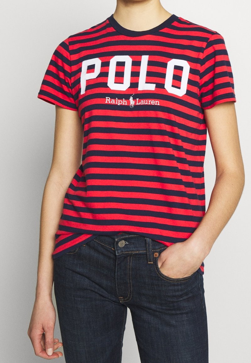 Röd och marinblå randig t-shirt med kort ärm och rund halsringning. Har stor vit text "POLO" och "Ralph Lauren"-logotypen i mitten.