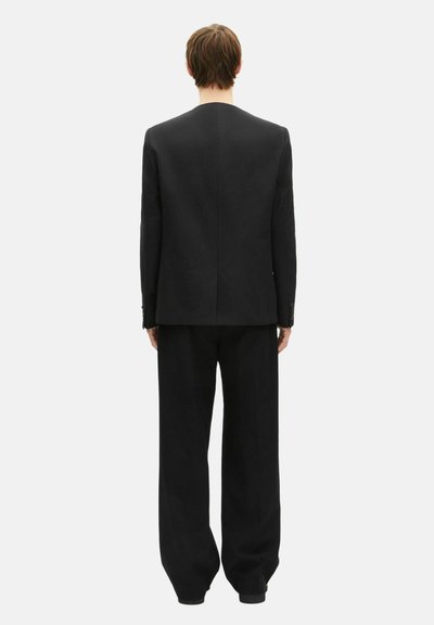 Abito nero composto da una giacca su misura e pantaloni a vestibilità ampia, caratterizzato da un design pulito e dettagli minimi. Tessuto dalla texture liscia.
