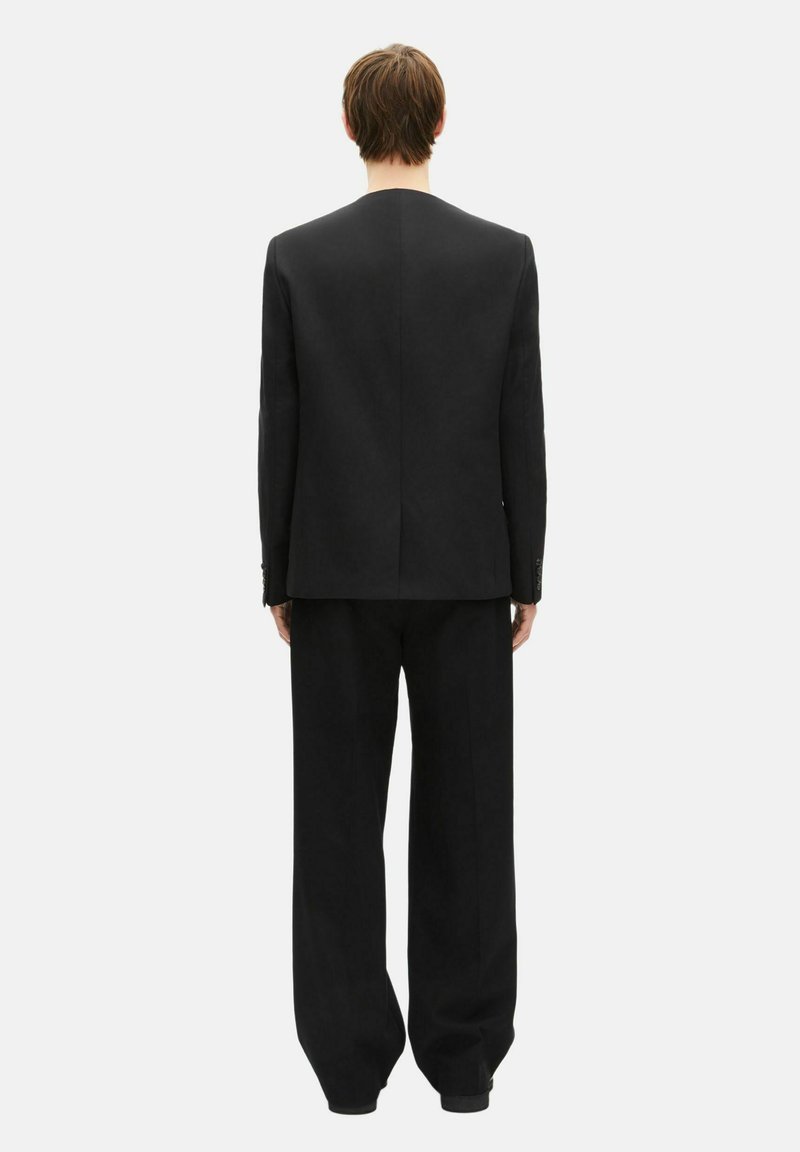 Black suit comprised of a tailored jacket and loose-fit trousers, featuring a clean design and minimal detailing. Smooth fabric texture.