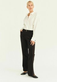 Camicia bianca a maniche lunghe con bottoni abbinata a pantaloni neri a vita alta e scarpe nere basse; presenta un colletto arrotondato e una vestibilità rilassata.