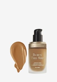 Foundation bottle with a clear base, gold accents, and a black pump. Next to it, a smooth, medium brown foundation swatch.