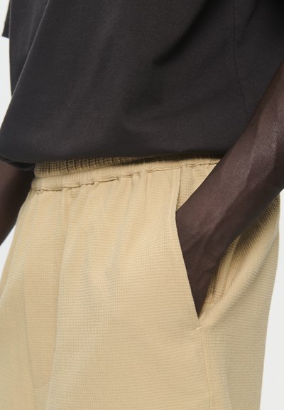 Chemise noire à manches courtes associée à un short beige texturé avec une taille élastique et des poches latérales.