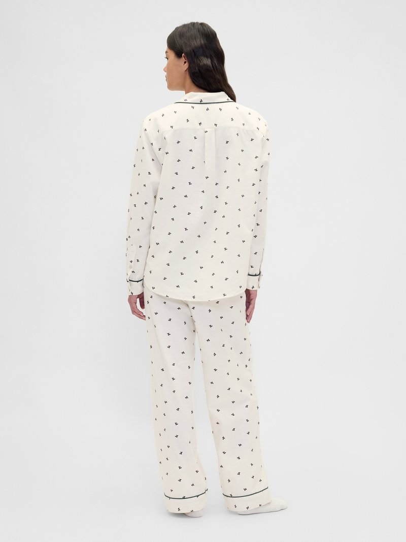 Ensemble de pyjama couleur crème avec des motifs floraux noirs. Comprend une chemise à col et un pantalon à jambes larges avec un passepoil contrastant le long des bords.