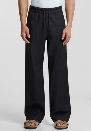 Czarne spodnie o szerokich nogawkach z elastycznym pasem i regulowanym sznurkiem. Wykonane z miękkiego materiału, o gładkiej teksturze.
