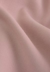 Weicher, strukturierter Stoff in einem gedämpften Rosaton, der subtilen Stretch und eine glatte Oberfläche zeigt, mit feinen Webdetails, die überall sichtbar sind.