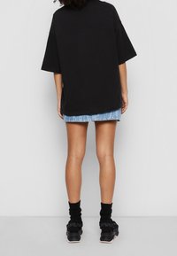 T-shirt nera over-size a maniche corte, abbinata a una gonna di jeans. Sneakers nere e calzini neri a costine completano l'outfit.