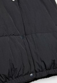 Tissu rembourré noir avec boutons pression et ourlet élastiqué, montrant un gros plan d'une section de veste matelassée.