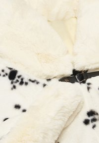 Cappotto in pelliccia sintetica di colore crema con macchie nere. Caratterizzato da una texture morbida, colletto ampio e una cintura nera con fibbia in metallo. Interno foderato.