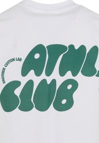 Bílá bavlněná trička s oversized zeleným textem ve tvaru bublin, který na zádech zní "ATNL CLUB" a "ANOTHER COTTON LAB" v kruhovém designu.