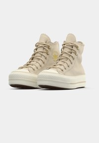 Beige høye sneakers laget av teksturert stoff med gull detaljer, med en hvit gummisåle og rund tå. Stjerne-logo på siden.