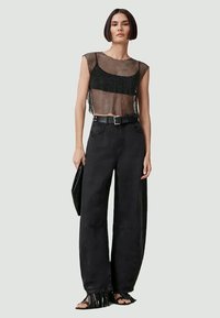 Top corto in rete nera con maniche corte, abbinato a pantaloni neri larghi, una cintura nera e una borsa a tracolla nera. Sandali piatti con dettagli in frange.