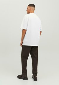 Hvid bomulds t-shirt med en afslappet pasform, korte ærmer og rund hals, parret med mørkebrune tapered bukser og sorte snørebåndsko.