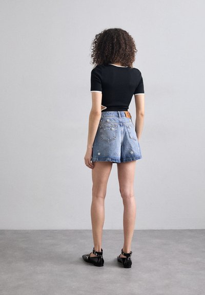 Top nero a maniche corte con bordatura bianca; pantaloni corti in denim azzurro chiaro con decorazioni floreali; ballerine nere con cinturini. Modella di spalle.