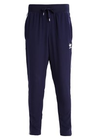 Marinblå joggerbyxor med elastisk midja och dragsko. Har vitt Adidas-logotyp och sidostickningar. Mjuk tyg med en avsmalnande design.