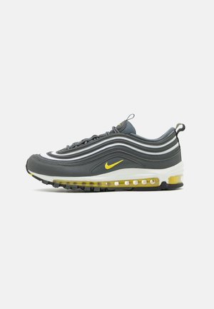 Baskets Nike Air Max 97 gris foncé avec des accents jaunes, semelle intermédiaire blanche et amorti visible à air sur un fond clair uni.