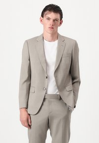 Blazer cinza-claro combinado com calças a condizer, apresenta um design de um só botão, lapelas recortadas e dois bolsos frontais. T-shirt branca de gola redonda por baixo.