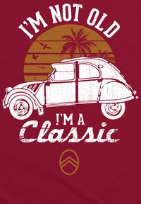 Červené tričko s bílou ilustrací vintage auta, palmami a západem slunce. Nápis zní "NEJSEM STARÝ, JSEM KLASIKA." Obsahuje logo Citroën.