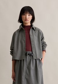 Siva majica s prugicama, dugih rukava, opuštenog kroja, složena preko tamnocrvene rebraste majice. Naglašena crnim pojasom i naboranom suknjom.