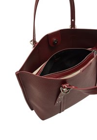 Czerwona torba tote z perforowanej skóry, z czarnym wnętrzem, podwójnymi uchwytami, kieszenią na zamek błyskawiczny i zapięciem na magnes. Zdobiona srebrnym okuciem.