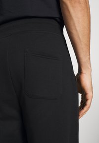 Zwarte sweatpants met een elastische tailleband en een achterzak. De stof lijkt zacht en mat, met minimale stikseldetails.